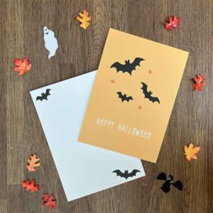 Oranje postkaart met zwarte vleermuizen en een witte envelop omgeven door herfstblaadjes van het merk Pinkstore