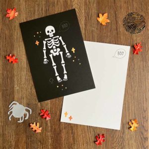 Zwarte postkaart met een wit skelet en witte envelop van het merk Pinkstore omgeven door herfstblaadjes