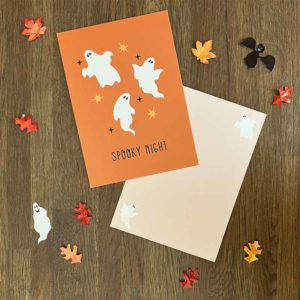 Oranje postkaart met drie witte spookjes en lichtroze envelop van het merk Pinkstore omgeven door herfstblaadjes